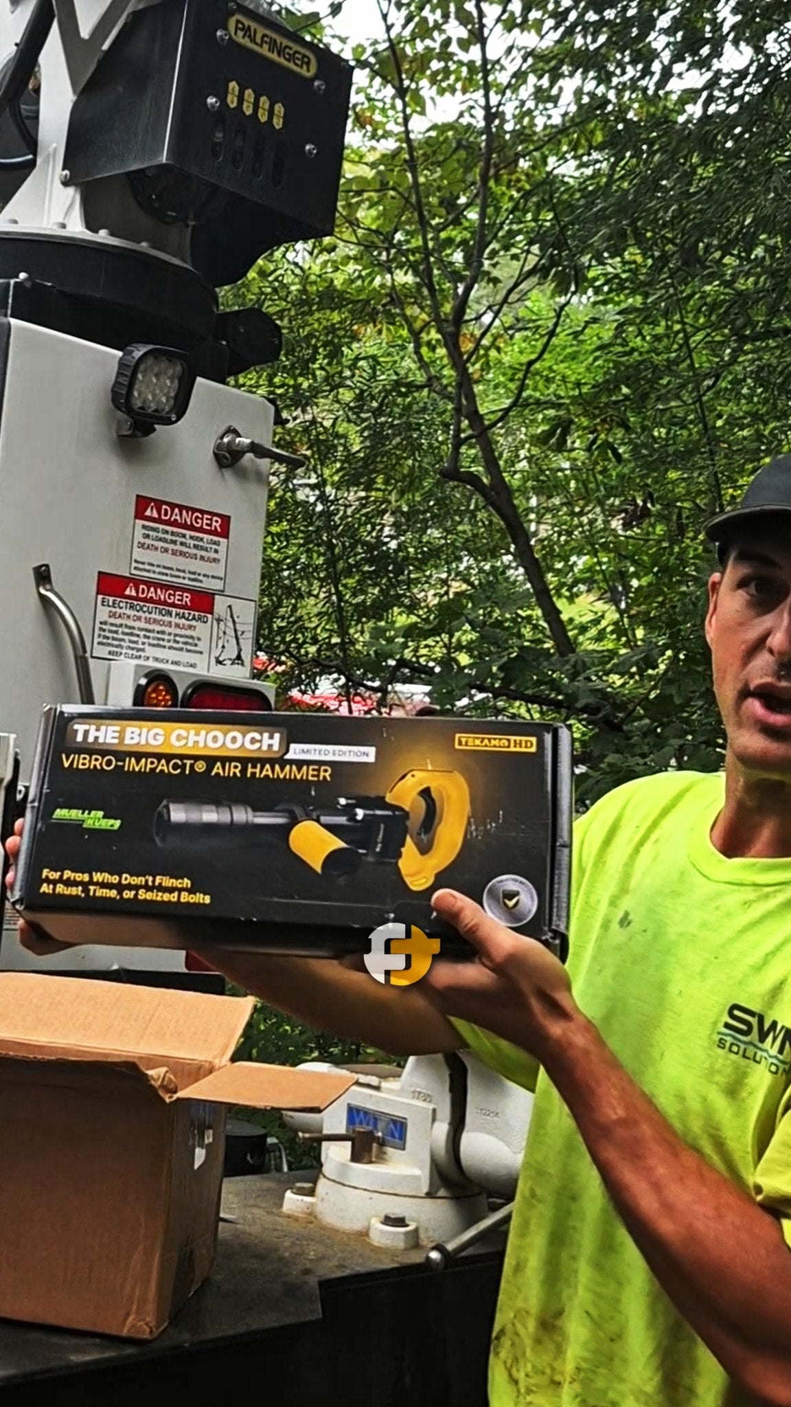 Technician holding a boxed Big Chooch Vibro-Impact Air Hammer outdoors near machinery.
