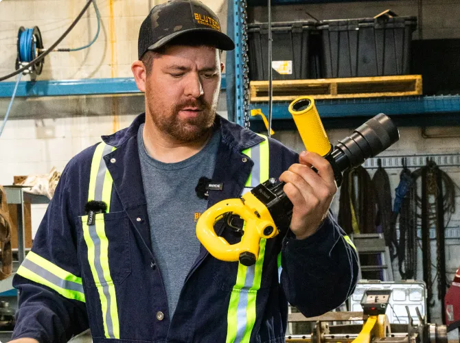 Mechanic inspecting and holding a yellow impact tool inside a workshop.