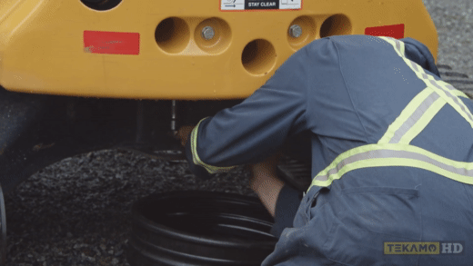 Mechanic demonstrates how to unscrew a drain plug on a mini excavator