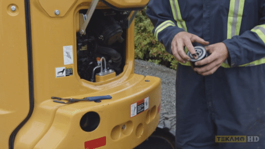 HD mechanic applies oil to the seal of an oil filter for a John Deere 35G