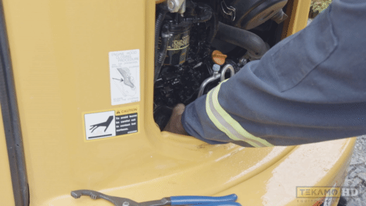 The mechanic is removing an old oil filter from inside a mini excavator