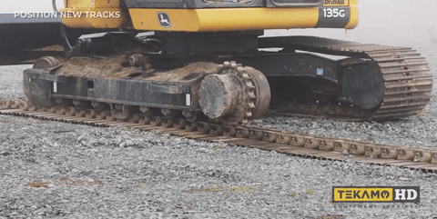 A John Deere 135G Excavator walks down from its old tracks to new steel tracks with rubber pads.
