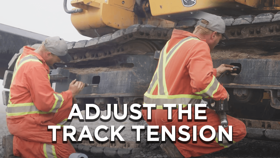 Heavy mechanic squatting next to the track of a large excavator