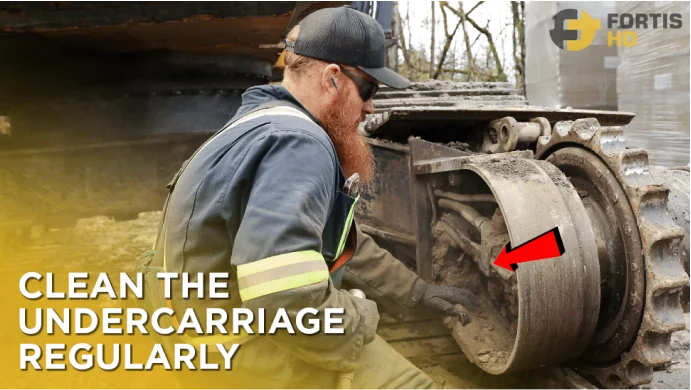 Heavy-duty mechanic cleaning caked dirt from a machine undercarriage.