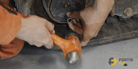A heavy-duty mechanic uses a manual impact driver to loosen a final drive drain plug