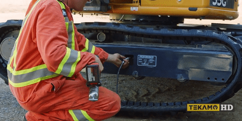 A heavy-duty mechanic adjusts the track tension on a mini excavator.