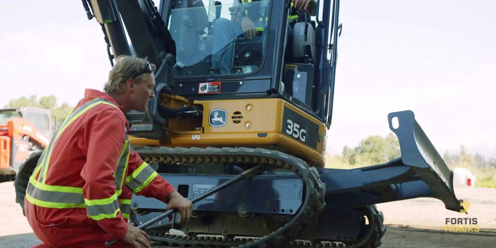 Heavy duty mechanic using a pry bar to pop a rubber track off a mini excavator