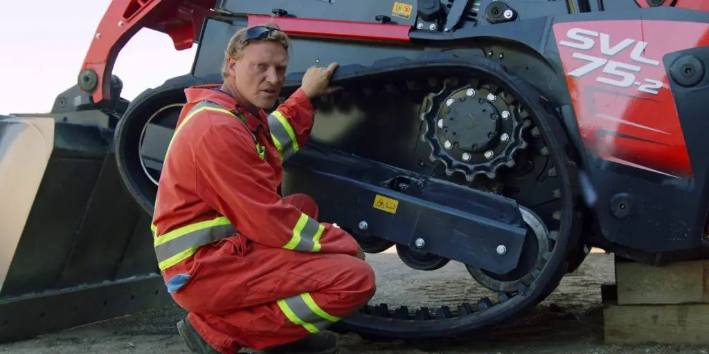 Heavy duty mechanic sitting in front of a Kubota CTL pointing to the grease valve
