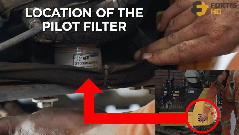A heavy-duty mechanic showing the location of the pilot filter. An overlay arrow shows a close-up of the filter.
