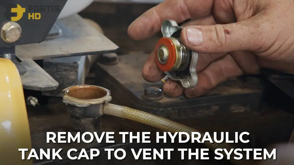 A heavy-duty mechanic vents the hydraulic oil system by removing the cap.