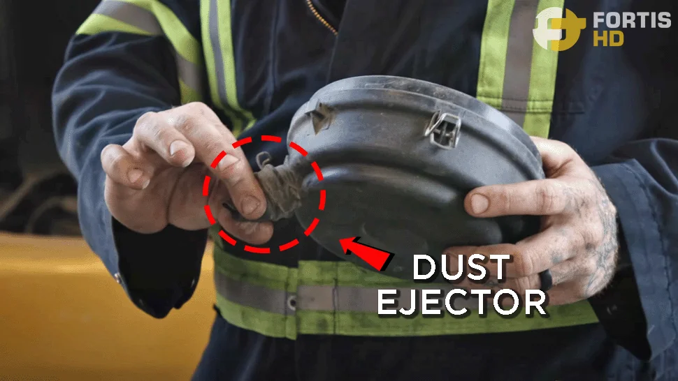 A heavy-duty mechanic holds an engine filter lid. An overlay arrow points at the dust ejector.