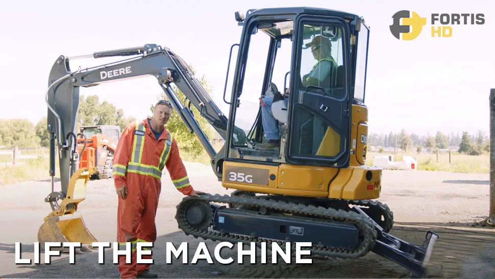 A heavy-duty mechanic uses the blade and bucket to lift a John Deere 35G mini excavator.