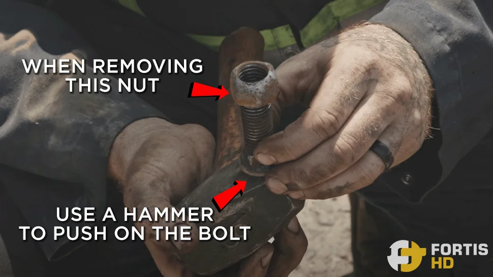 Heavy-duty mechanic shows how to use a hammer to hold the head of a worn bolt to remove the nut.