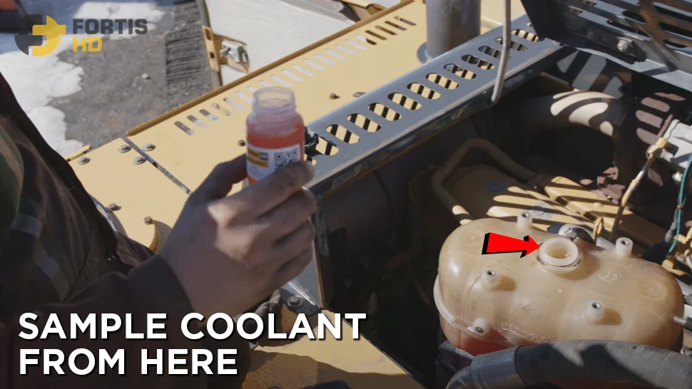 Heavy-duty mechanic holds a coolant sample from an excavator.