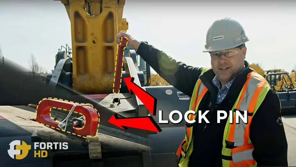 A heavy equipment operator shows the location and use of the attachment lock pin.