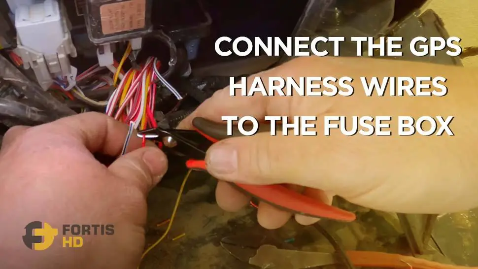 A heavy equipment operator connects the harness wires of a GPS to the fuse box on a John Deere 26G.