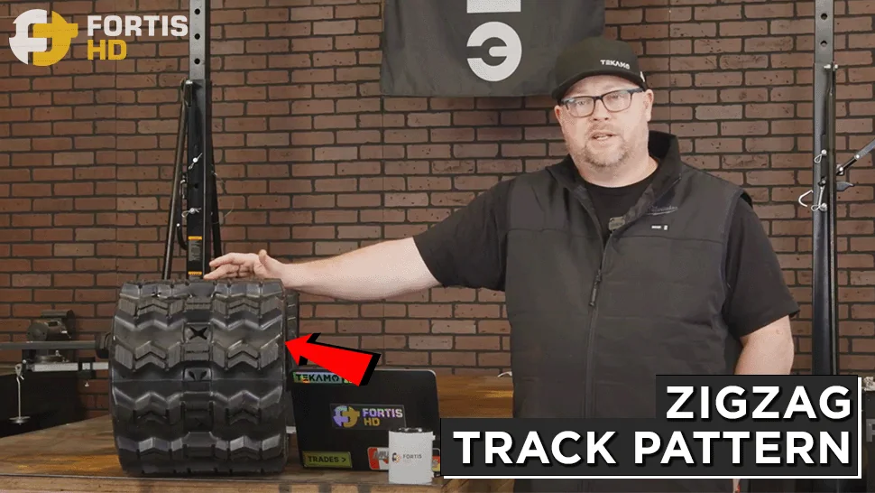 A heavy equipment technician shows a rubber track with a ZZ tread pattern.